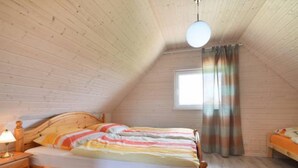 Une chambre mansardée chaleureuse, avec un lit en bois, une table de chevet, une fenêtre avec des rideaux et un plafond en pente.