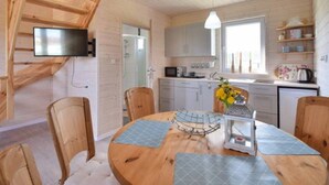 Un intérieur de chalet chaleureux avec un coin repas, des murs en bois et une cuisine dotée de meubles blancs.