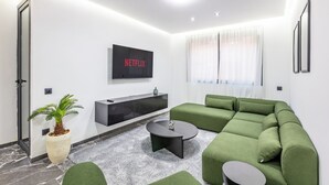 A modern living room with a green sofa, a coffee table, a flat-screen TV, and a potted plant. - Modern & cosy apartment with designer lounge - Ideal for a relaxing break (Marrakech Gueliz)