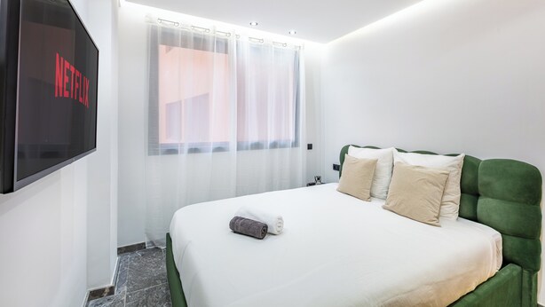 A hotel room with a bed, a TV screen displaying the Netflix logo, a window with sheer curtains, and a green upholstered headboard. - Modern & cosy apartment with designer lounge - Ideal for a relaxing break (Marrakech Gueliz)