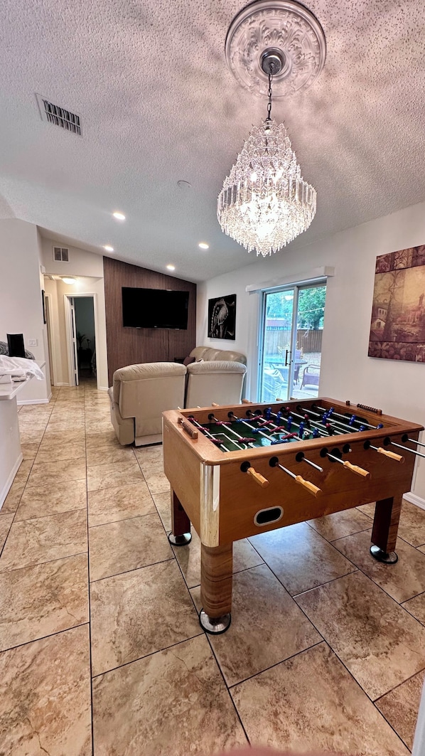 A room with a foosball table, a chandelier, and a television.