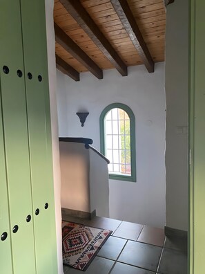 A staircase with a wooden ceiling, a window with a green frame, and a patterned rug on the floor. - El Olivarillo – Charming Accommodation for a Nature Getaway (Frigiliana)