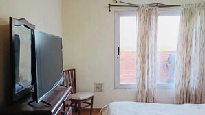 A hotel room with a bed, a TV on a wooden dresser, a chair, a window with curtains, and an air conditioning unit. - Bright Apartment with Green View, AC and WiFi - Close to the Beach Resort (Río Tercero)