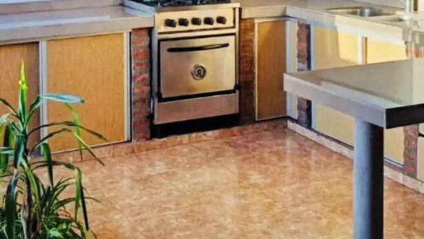 A kitchen with a gas stove, oven, and a water heater. There is a window with yellow curtains, a sink, and a potted plant. - Bright Apartment with Green View, AC and WiFi - Close to the Beach Resort (Río Tercero)