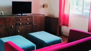 A room with a television, a wooden cabinet, and two blue ottomans. - Bright Apartment with Green View, AC and WiFi - Close to the Beach Resort (Río Tercero)