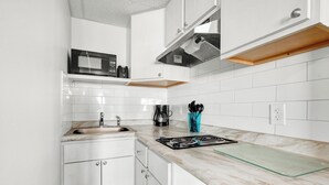 Una cocina moderna con gabinetes blancos, un lavamanos de acero inoxidable, un microondas, una cafetera y una estufa a gas.