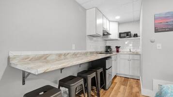 Une cuisine de taille réduite avec un plan de travail en marbre, des placards blancs et un plancher en bois.