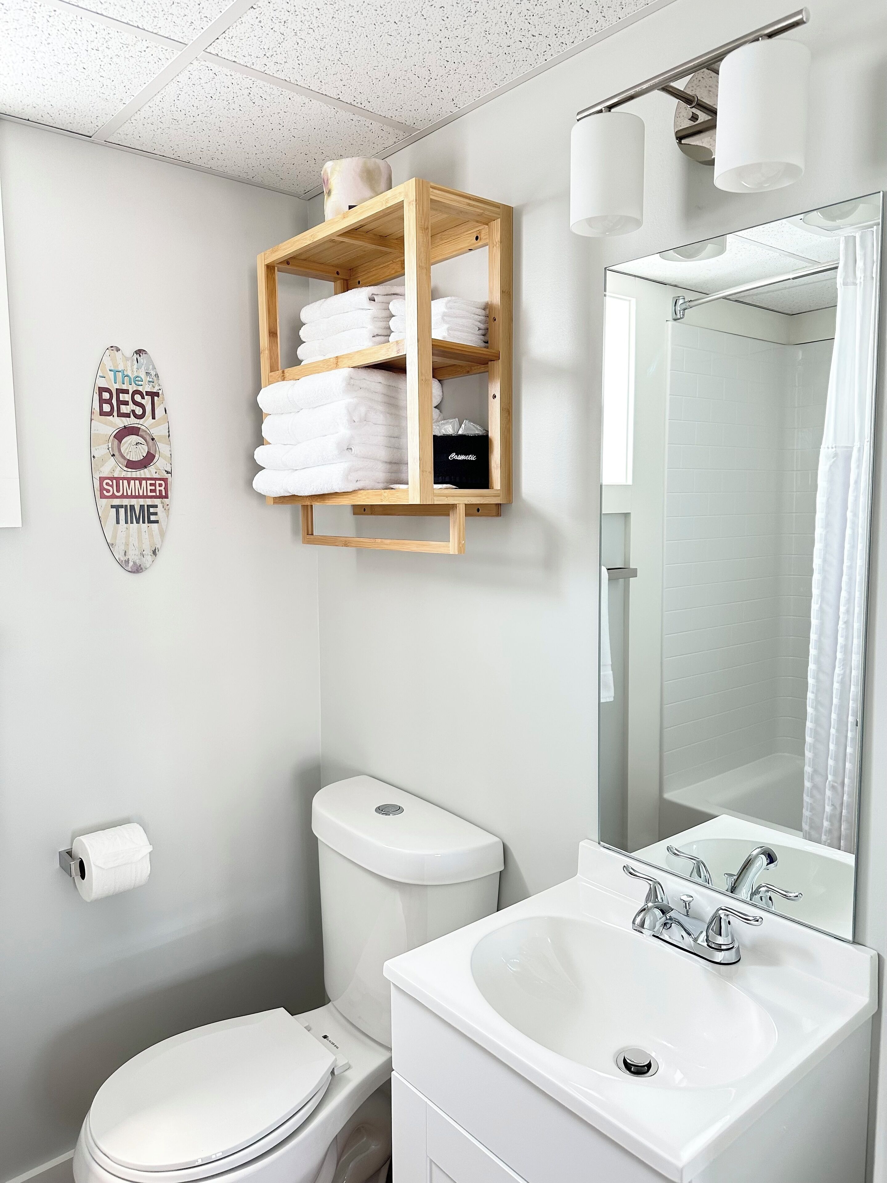 A modern bathroom with a toilet, sink, and shower. There is a towel rack with neatly folded towels and a sign that says "The BEST SUMMER TIME".