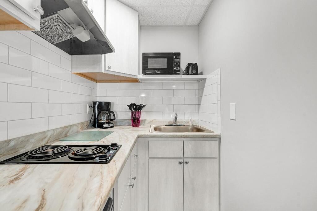 A kitchen with white tiled walls, a black microwave, a coffee maker, and a sink.