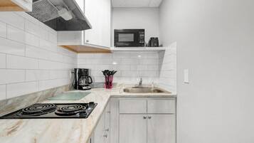 A kitchen with white tiled walls, a black microwave, a coffee maker, and a sink.