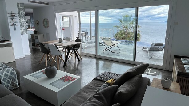 Una sala de estar moderna con un amplio ventanal corredera que da a un balcón con vistas al mar.