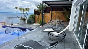 Zona de piscina al aire libre con sillones reclinables y vista al mar.