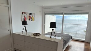 Un dormitorio con un ventanal grande, una cama, un aparador y dos lámparas.