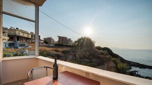 A balcony with a table and a bottle of wine, overlooking a coastal landscape with buildings and a clear sky. - SEA GEM APARTMENTS steps from the sand (Chania)