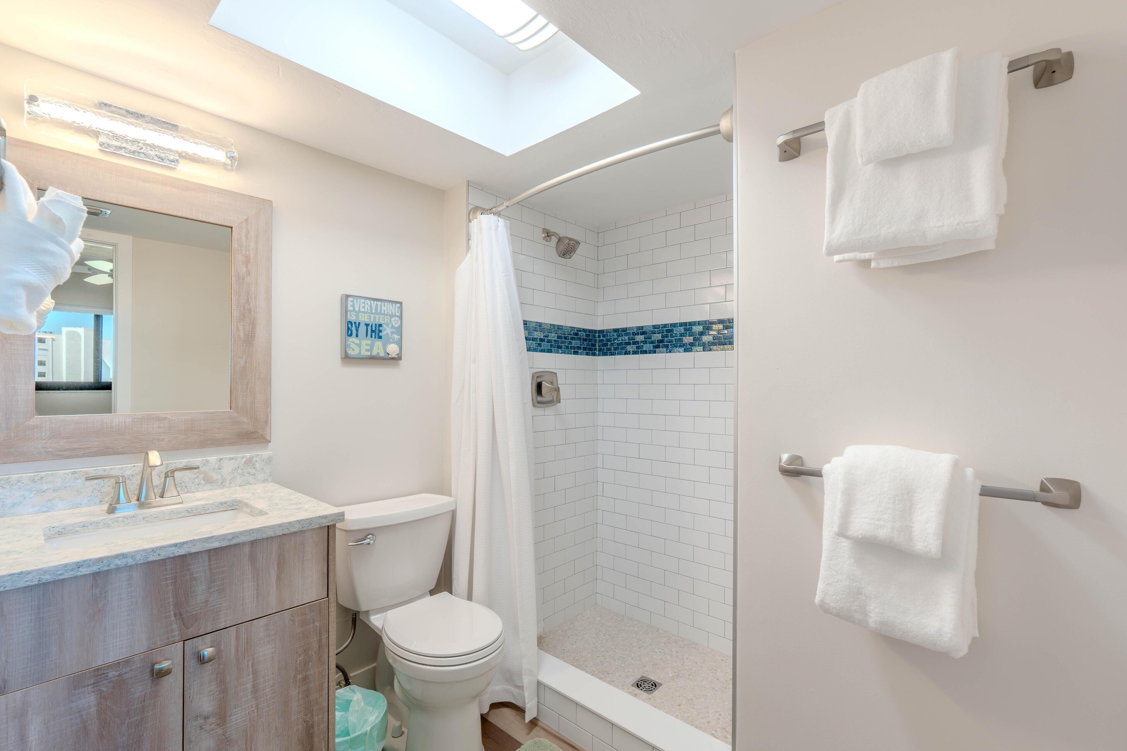 A modern bathroom with a skylight, a shower with blue tiles, a toilet, and a vanity with a mirror.