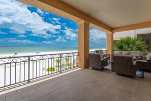 Un espacio al aire libre cubierto con vista a la playa, mobiliario de mimbre y una barandilla.