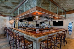 Un espace bar doté d’un comptoir en bois, de plusieurs tabourets de bar, d’un téléviseur et d’une décoration sur le thème du surf.