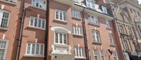 A row of red-brick townhouses with white window frames, a central entrance with a sign, and a black metal fence.