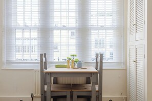 A room with a table and chairs near a window with blinds, a radiator below, and a door with louvered shutters. - Incredibly Located 1BDR Hideaway in Soho (Greater London)