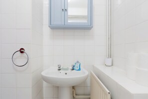 A bathroom with a white sink, a towel ring, a mirror above the sink, and a toilet paper holder on the wall. - Incredibly Located 1BDR Hideaway in Soho (Greater London)