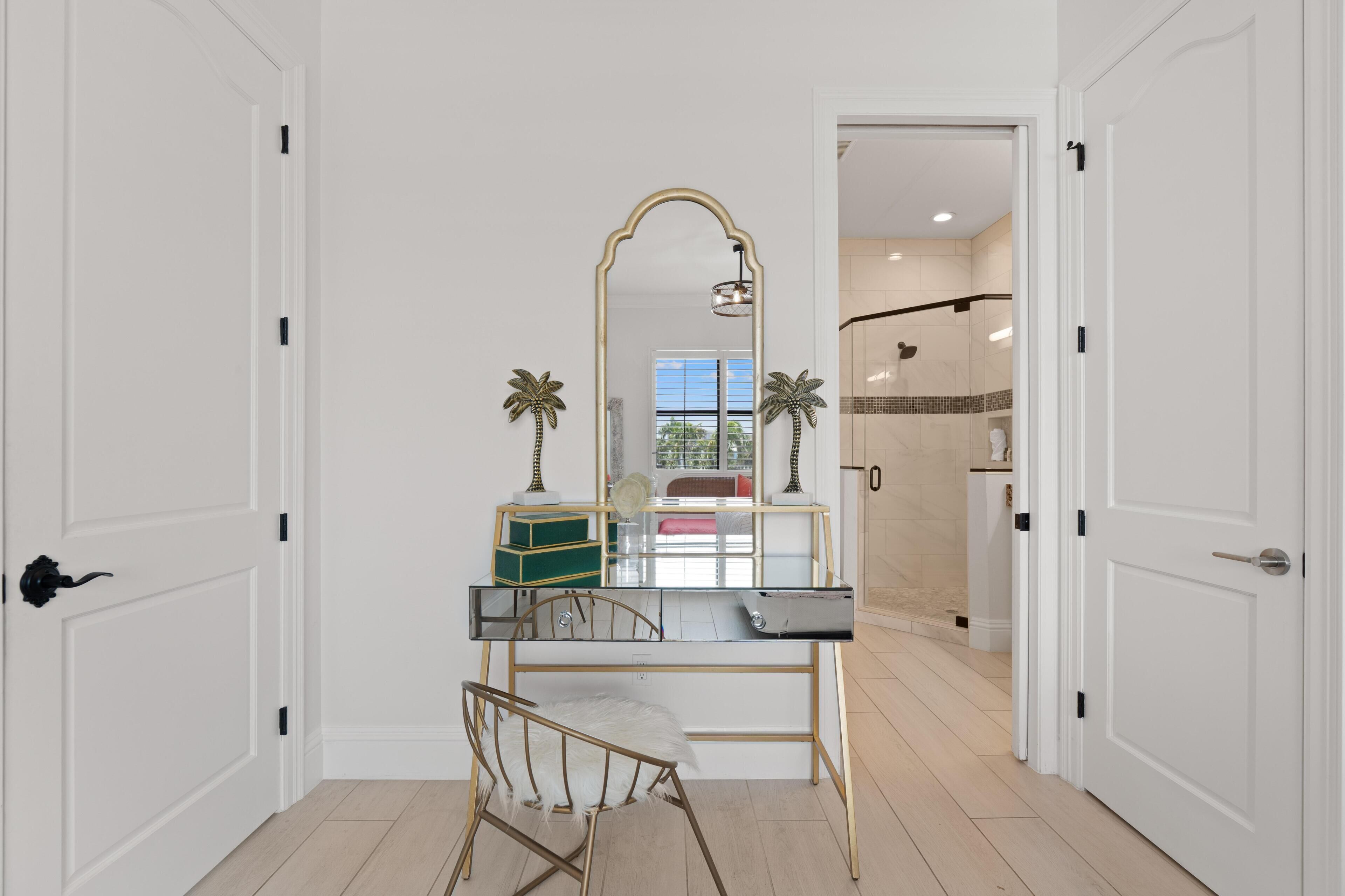 A room with a desk, chair, mirror, and a view of a bathroom with a shower.