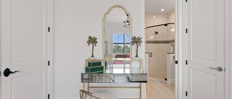 A room with a desk, chair, mirror, and a view of a bathroom with a shower.