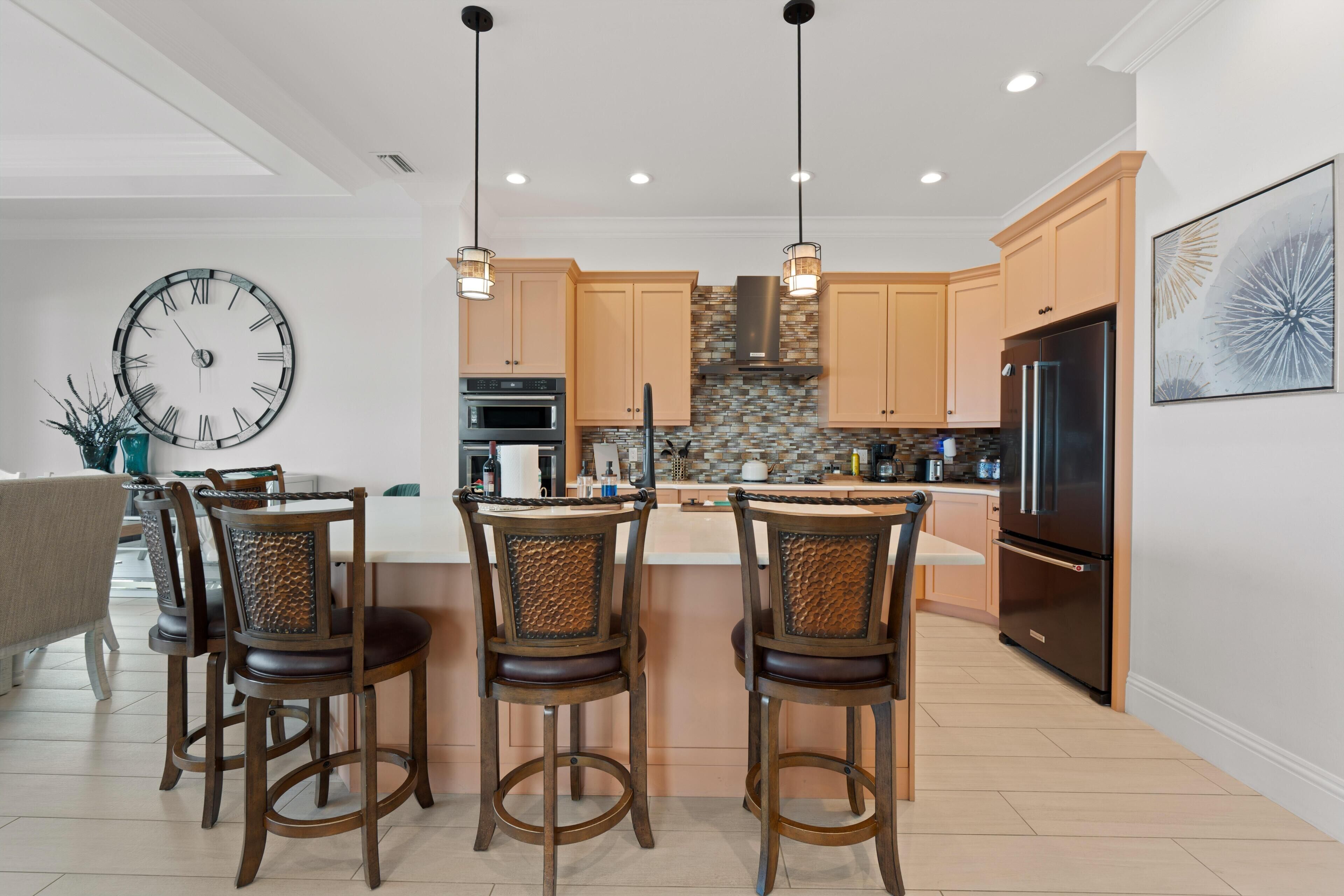 A modern kitchen with a central island, pendant lights, and a clock on the wall.
