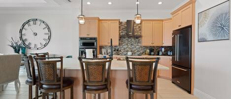 A modern kitchen with a central island, pendant lights, and a clock on the wall.