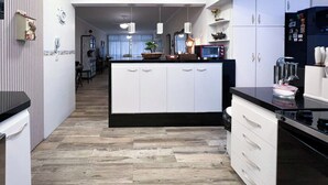 A modern kitchen with white cabinets, a central island, and a black countertop. - Apartamento Enseada 24 (Guarujá)