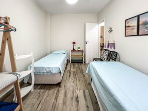 Pieni huone, jossa on kaksi erillistä sänkyä, puinen tuoli, pieni pöytä lampun kanssa ja hylly, jossa on koriste-esineitä.