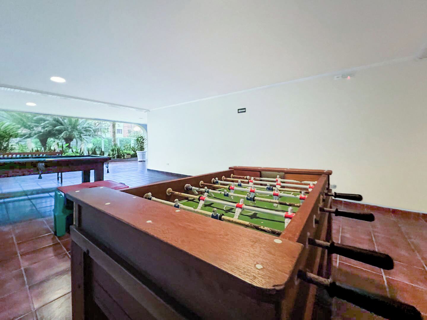 A foosball table in a room with a large window, a pool table, and a tiled floor.