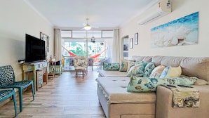 A living room with a sofa, TV, and a hammock. - Apartamento Enseada 24 (Guarujá)