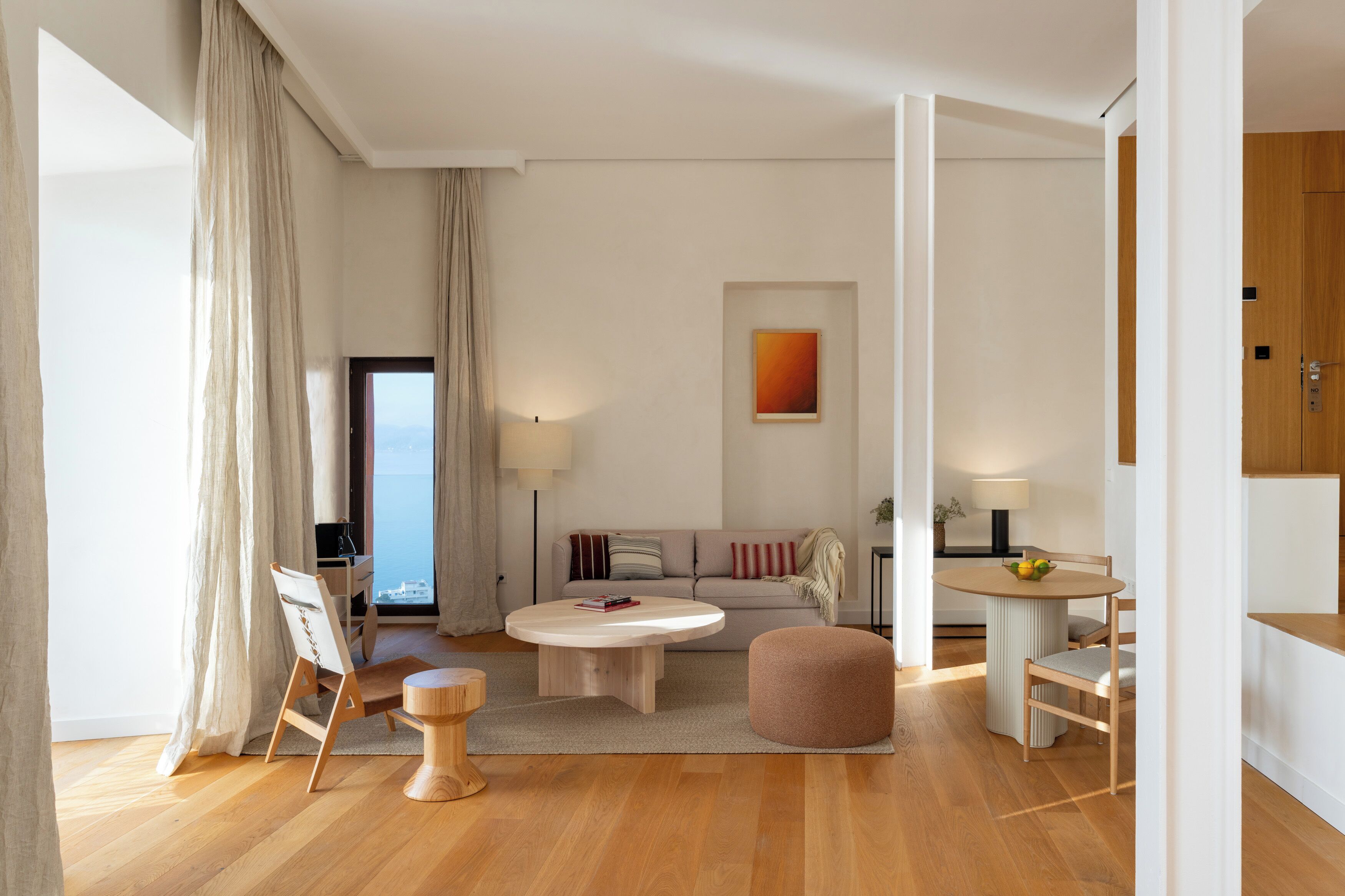 Een moderne woonkamer met een ronde salontafel, een bank, een eettafel met stoelen en een groot raam met gordijnen.