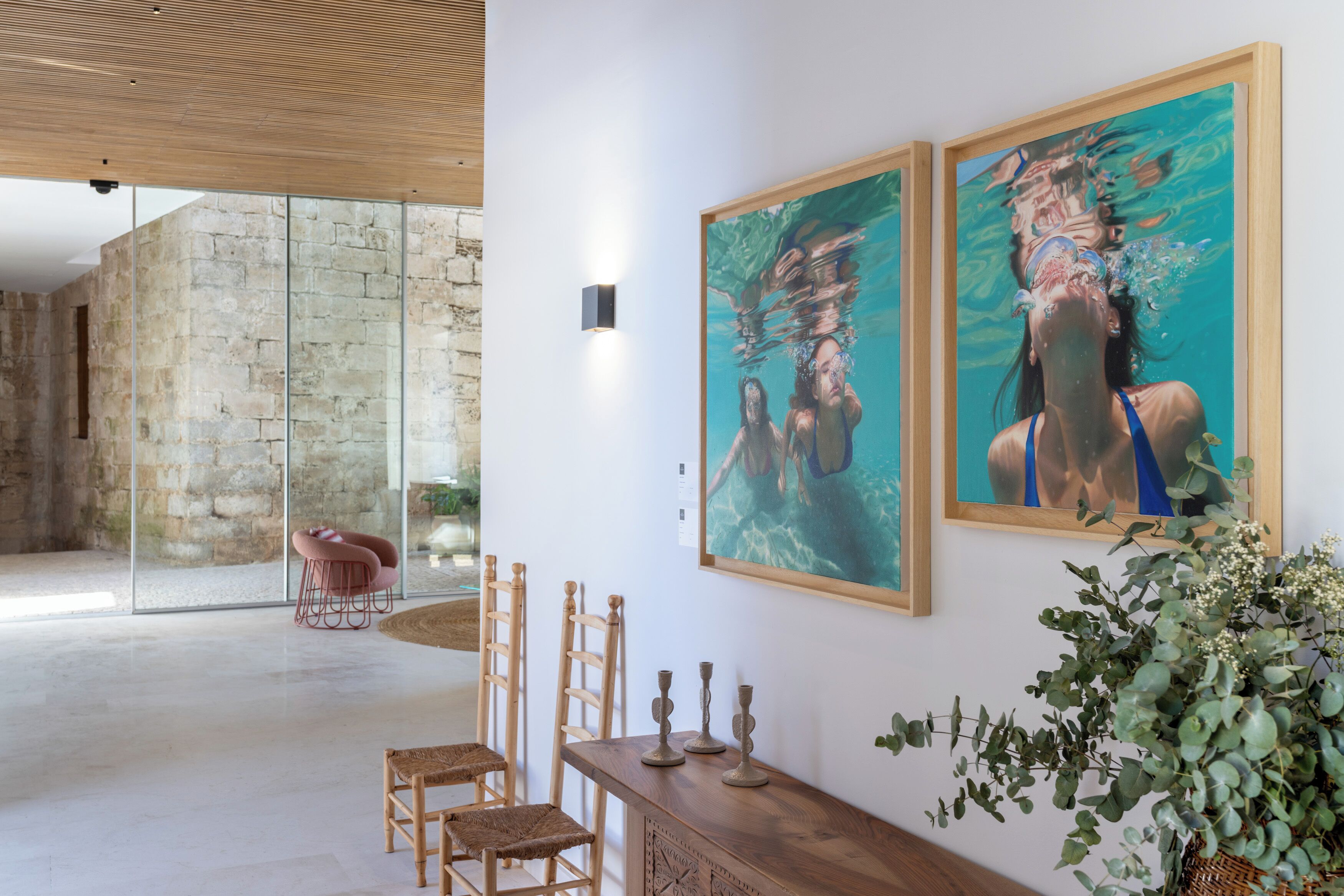 Una habitación amplia con pared de piedra, un separador de vidrio y una mesa de madera con sillas.