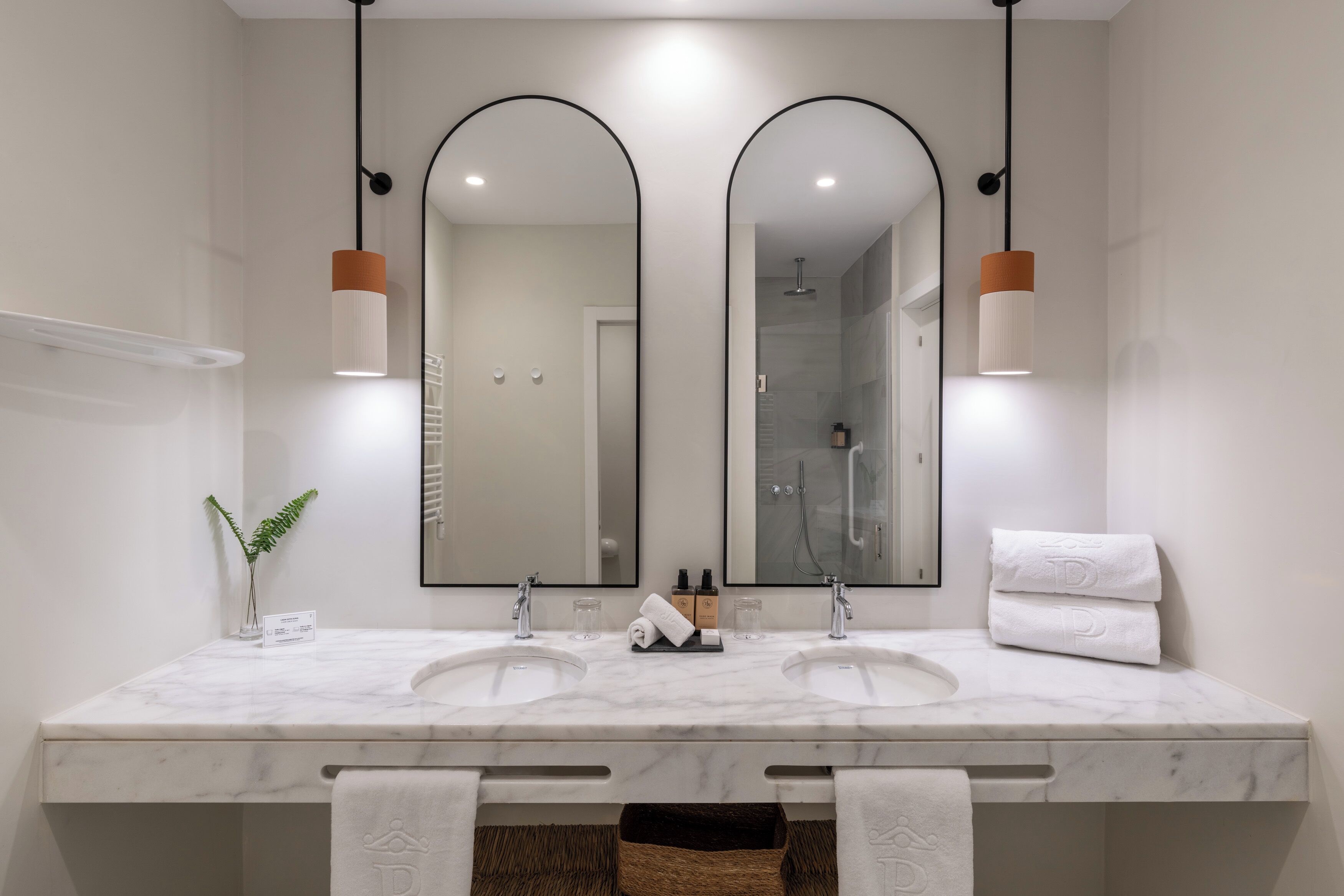 Un baño moderno con dos lavamanos, un espejo grande y lámparas colgantes.
