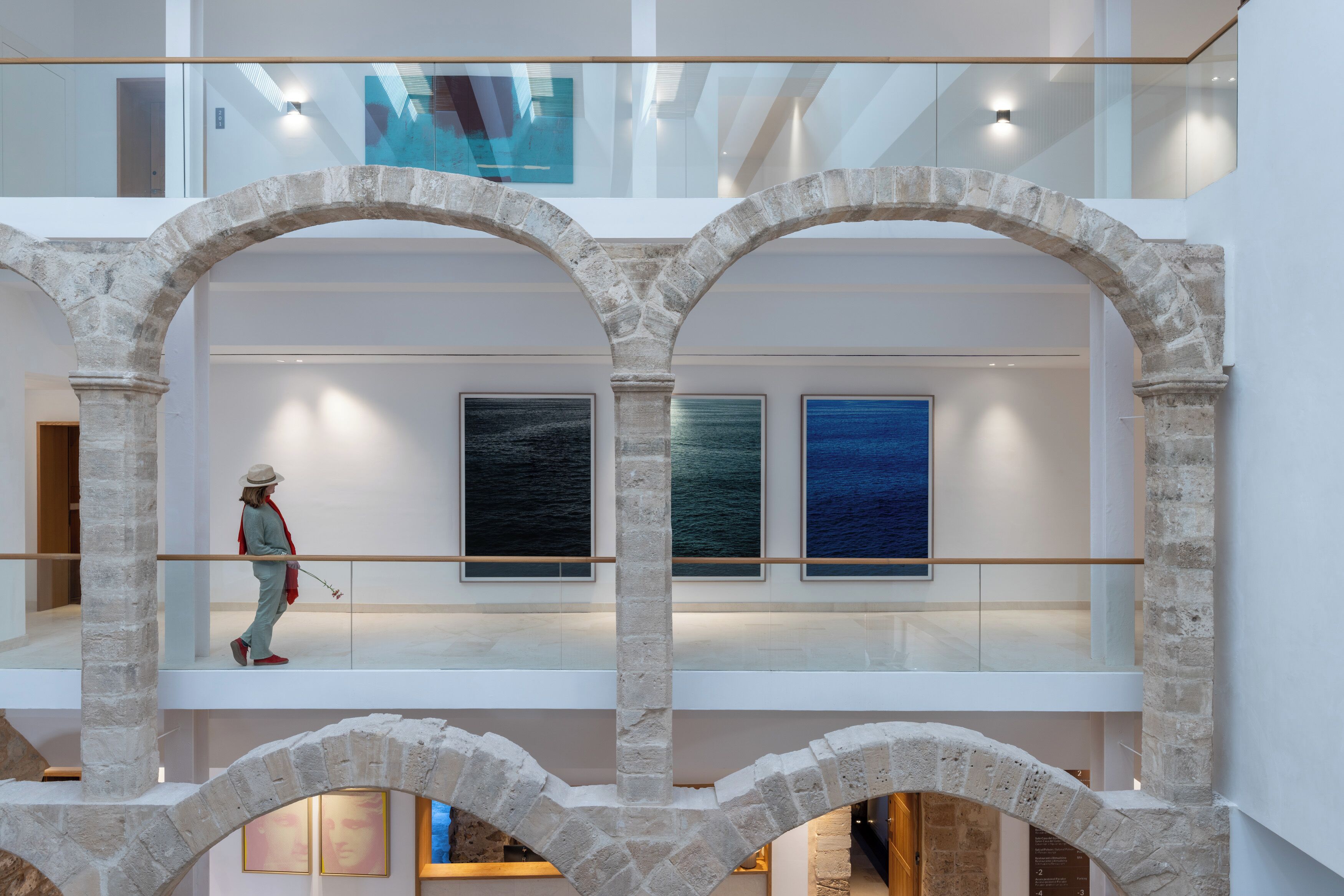 A multi-level atrium with stone arches, artwork on the walls, and a person walking.