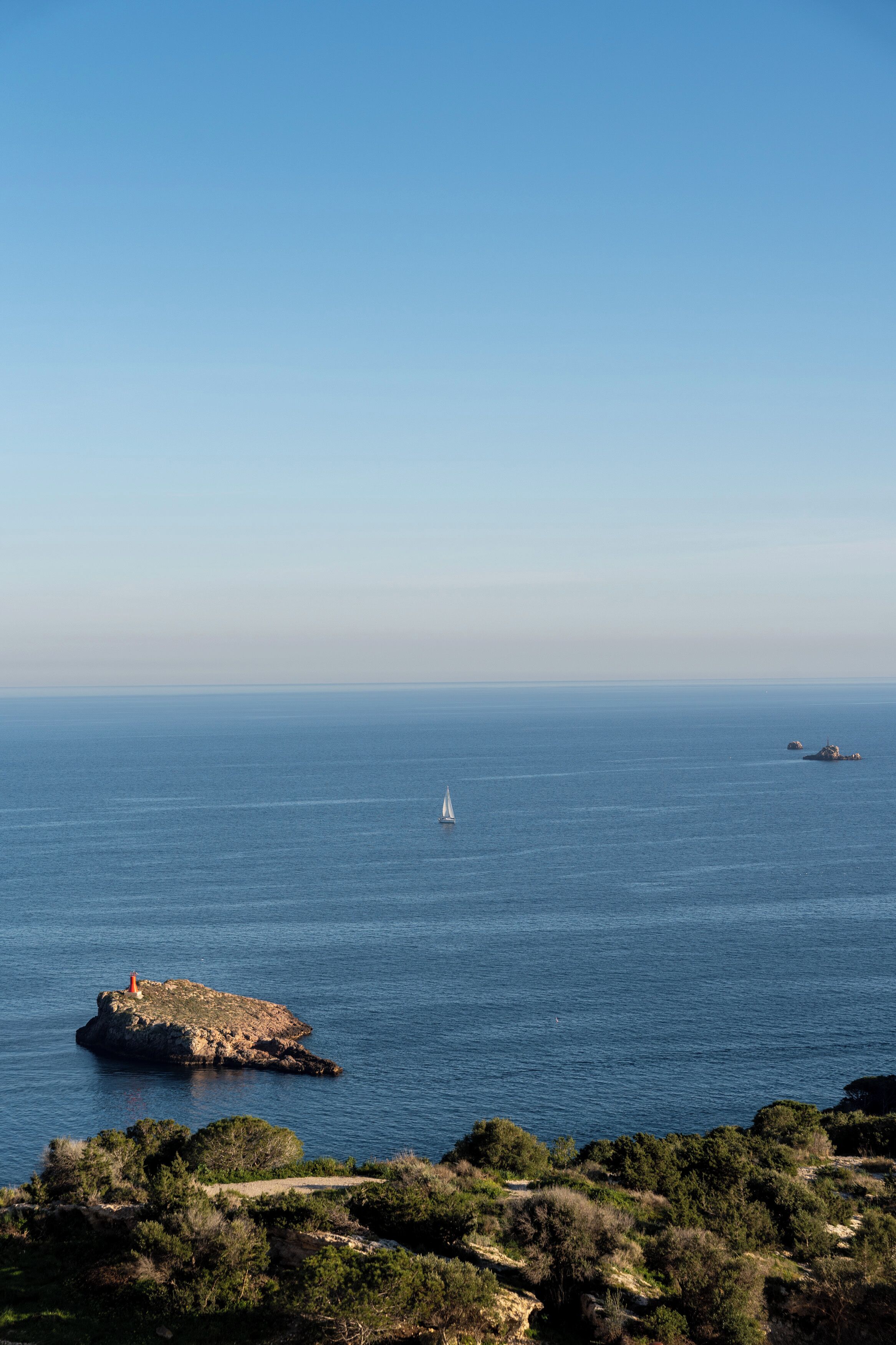 A coastal landscape with a rocky outcrop and a sailboat in the distance.