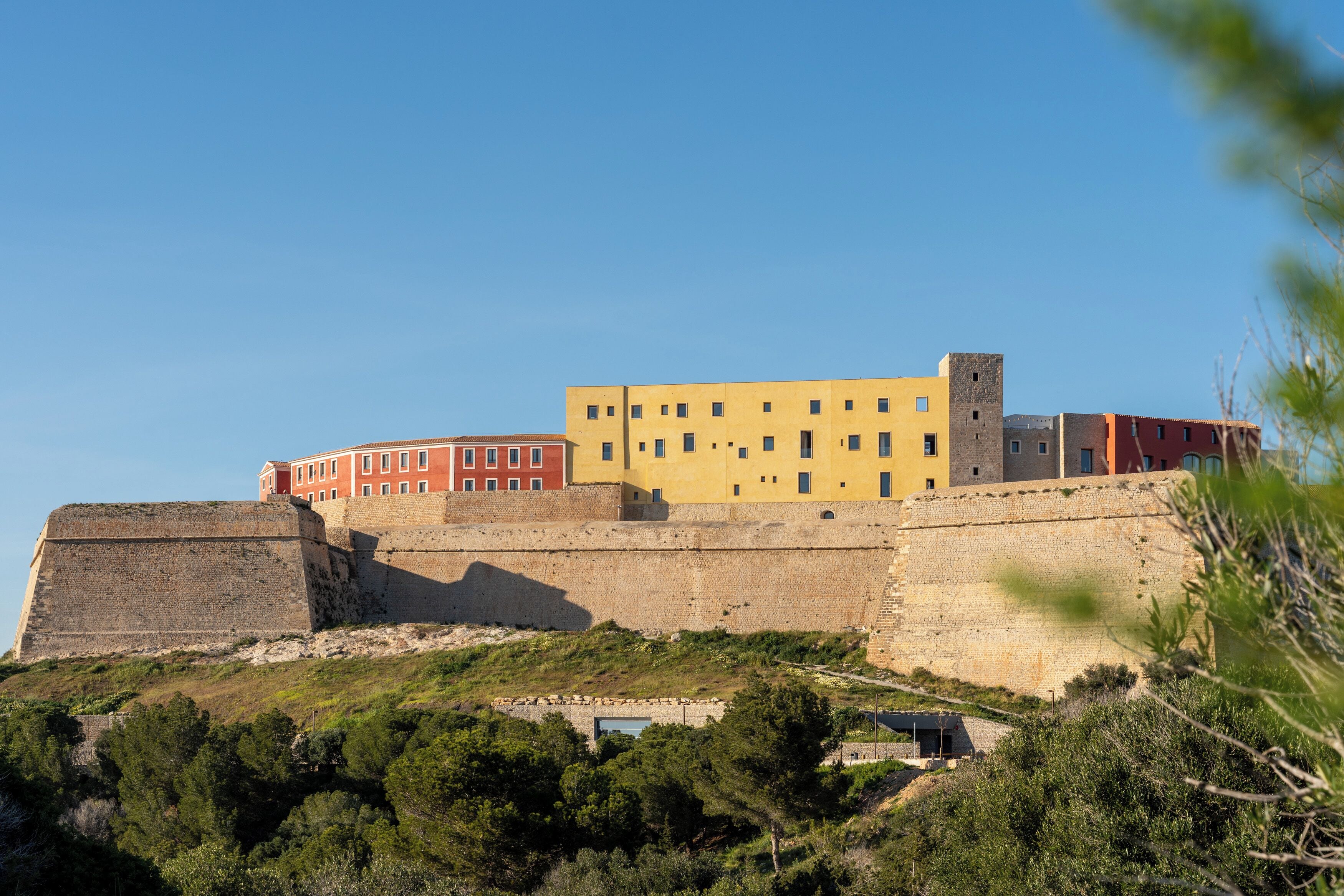 Un edificio histórico con una fortificación destacada, una estructura amarilla de techos planos y un edificio rojo con múltiples ventanas.