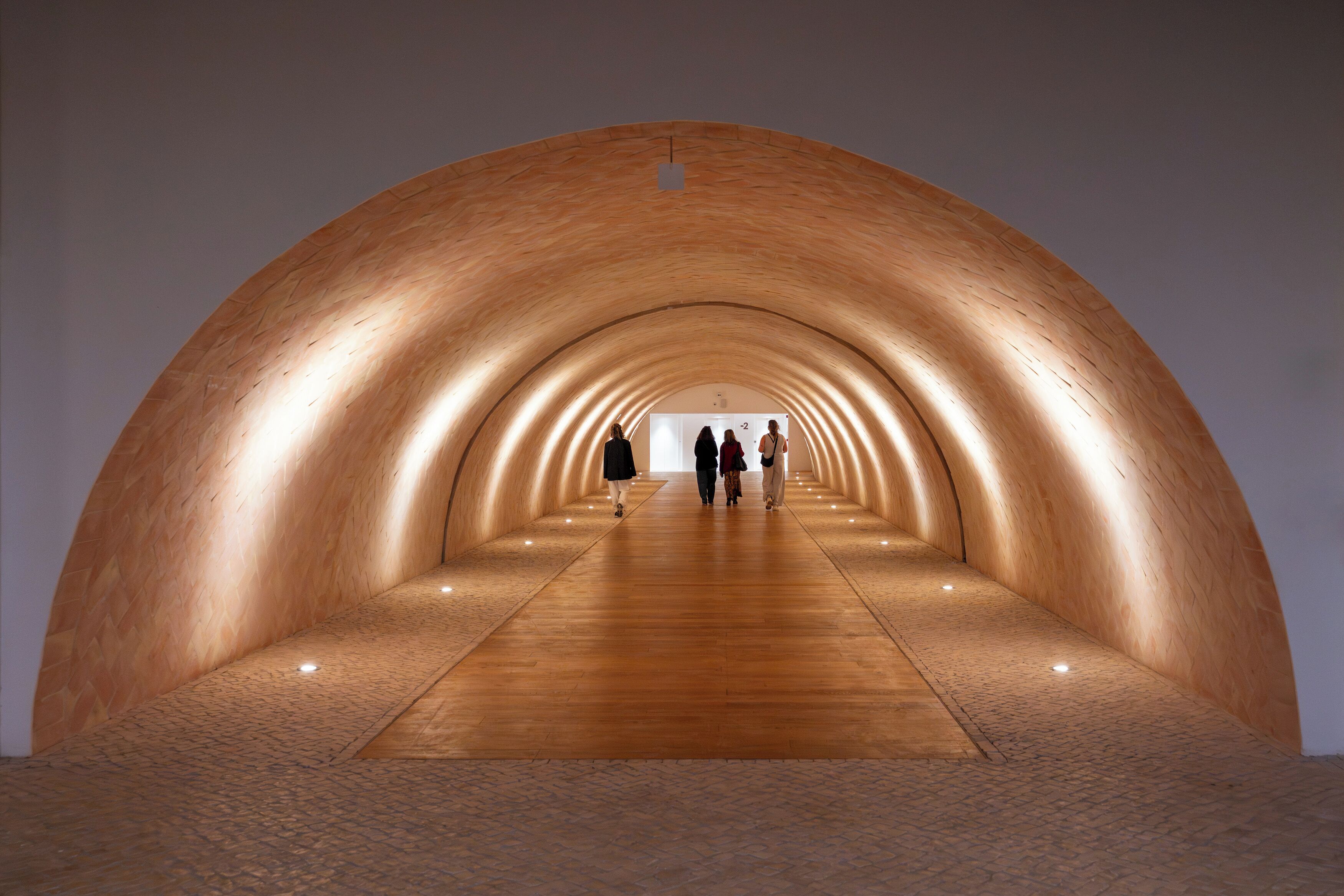 A tunnel-like structure with a wooden floor and walls, illuminated by ceiling lights.