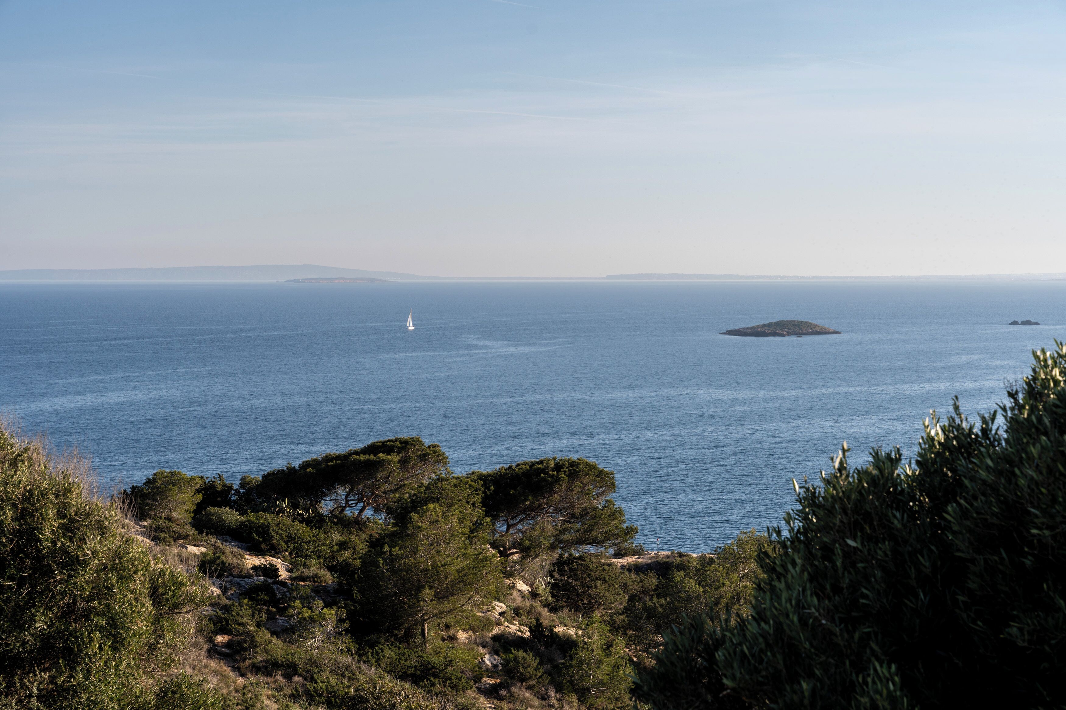 Un paisaje costero con vista al mar, un velero y tierra distante.