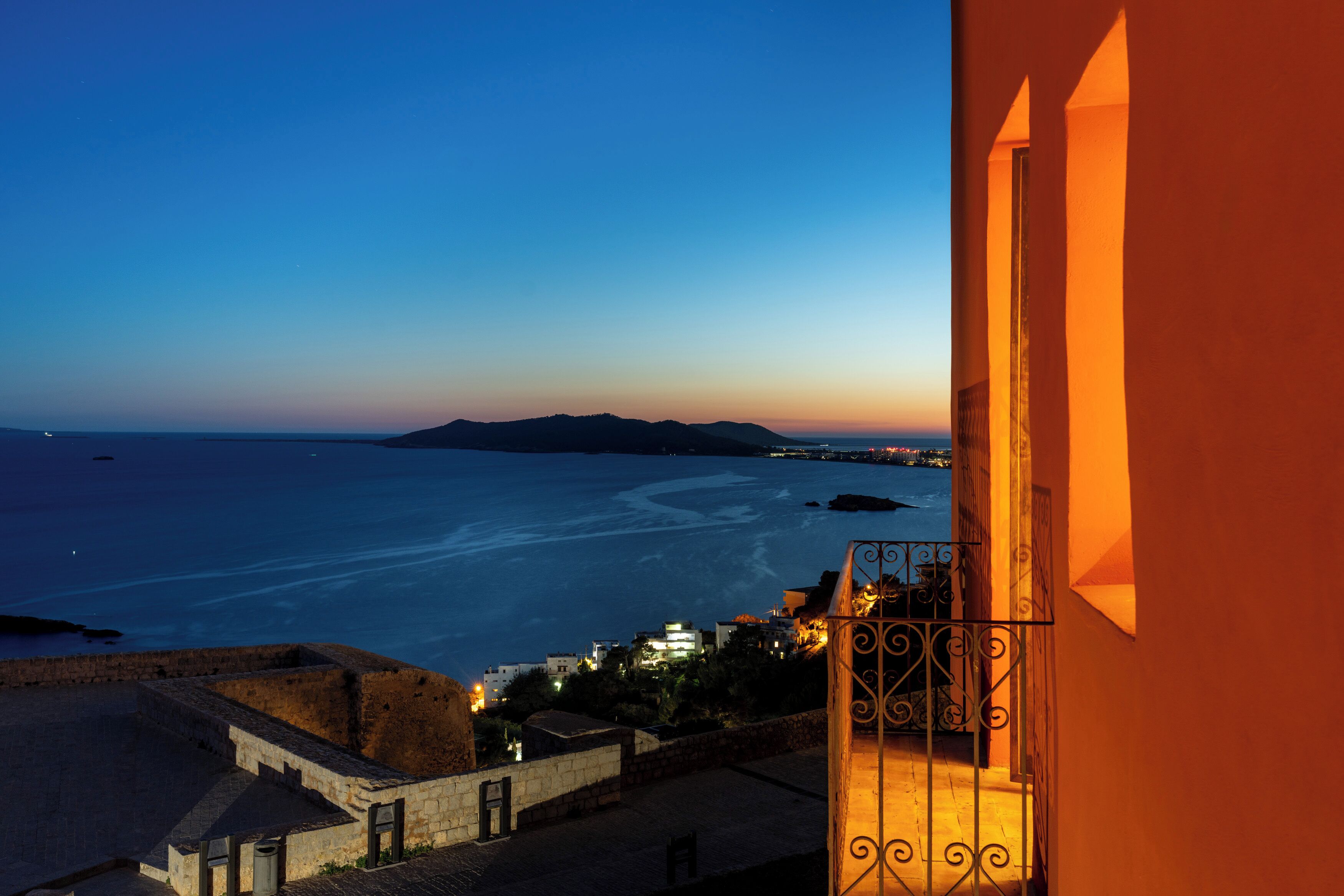 A coastal view from a balcony with a stone wall and a metal railing.