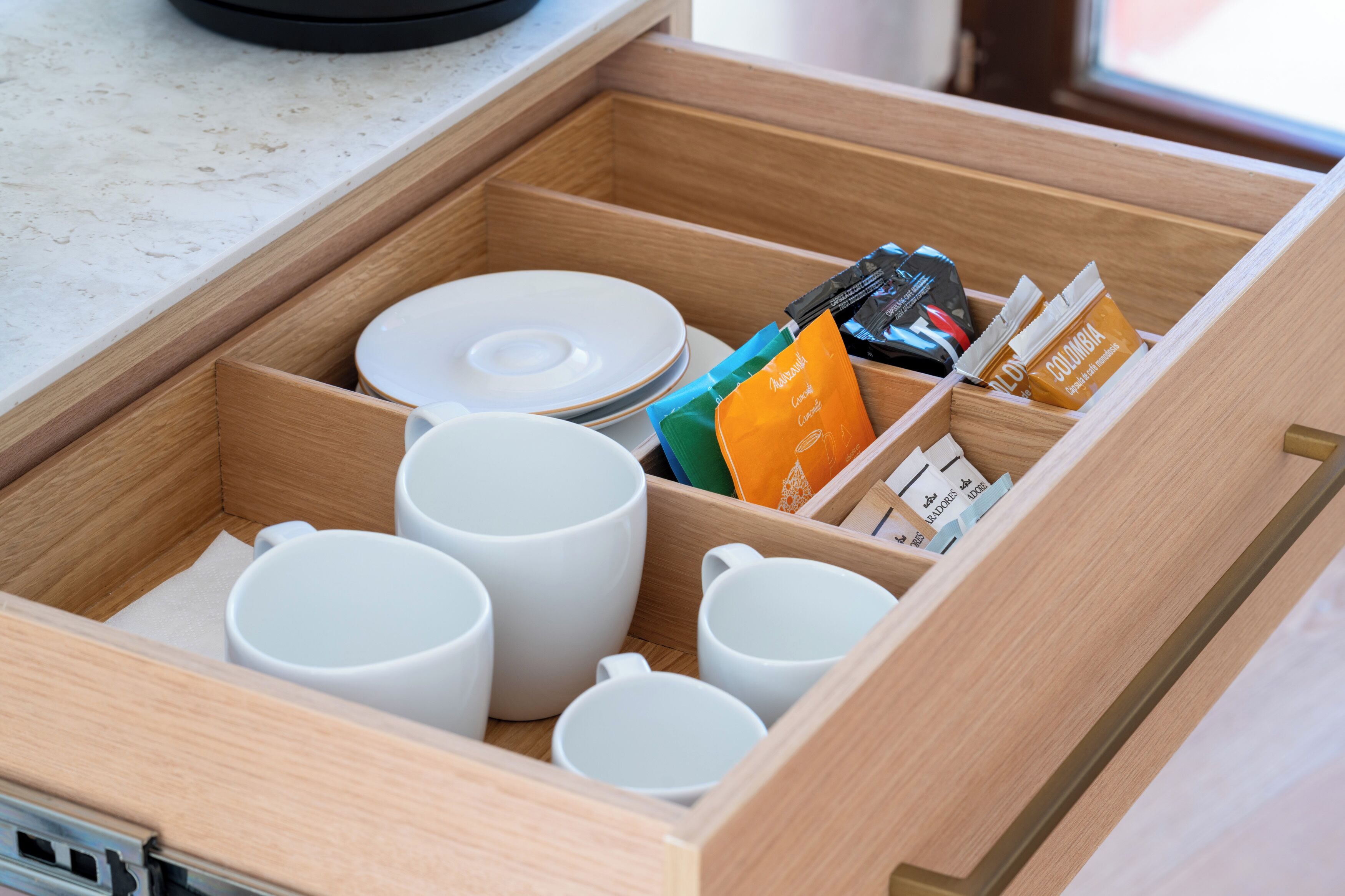 A drawer with white mugs, plates, and food packets.