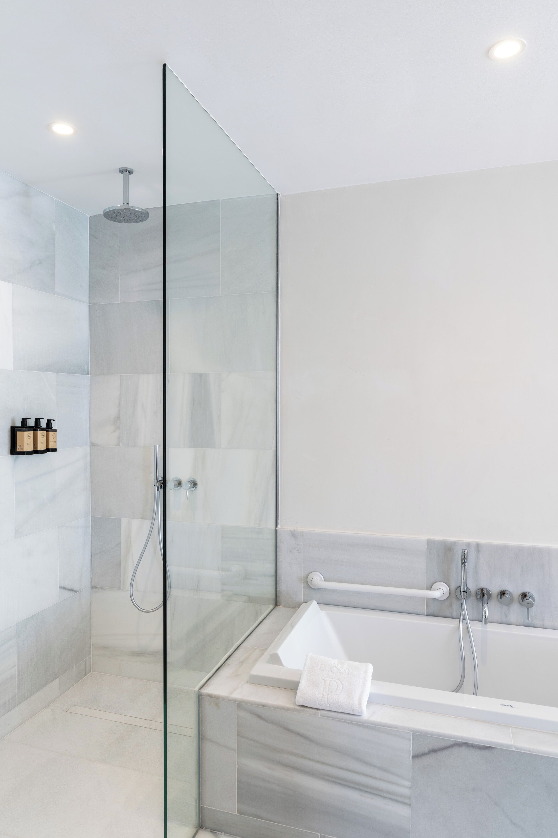 A modern bathroom with a glass-enclosed shower, a marble-tiled vanity, and a white bathtub.