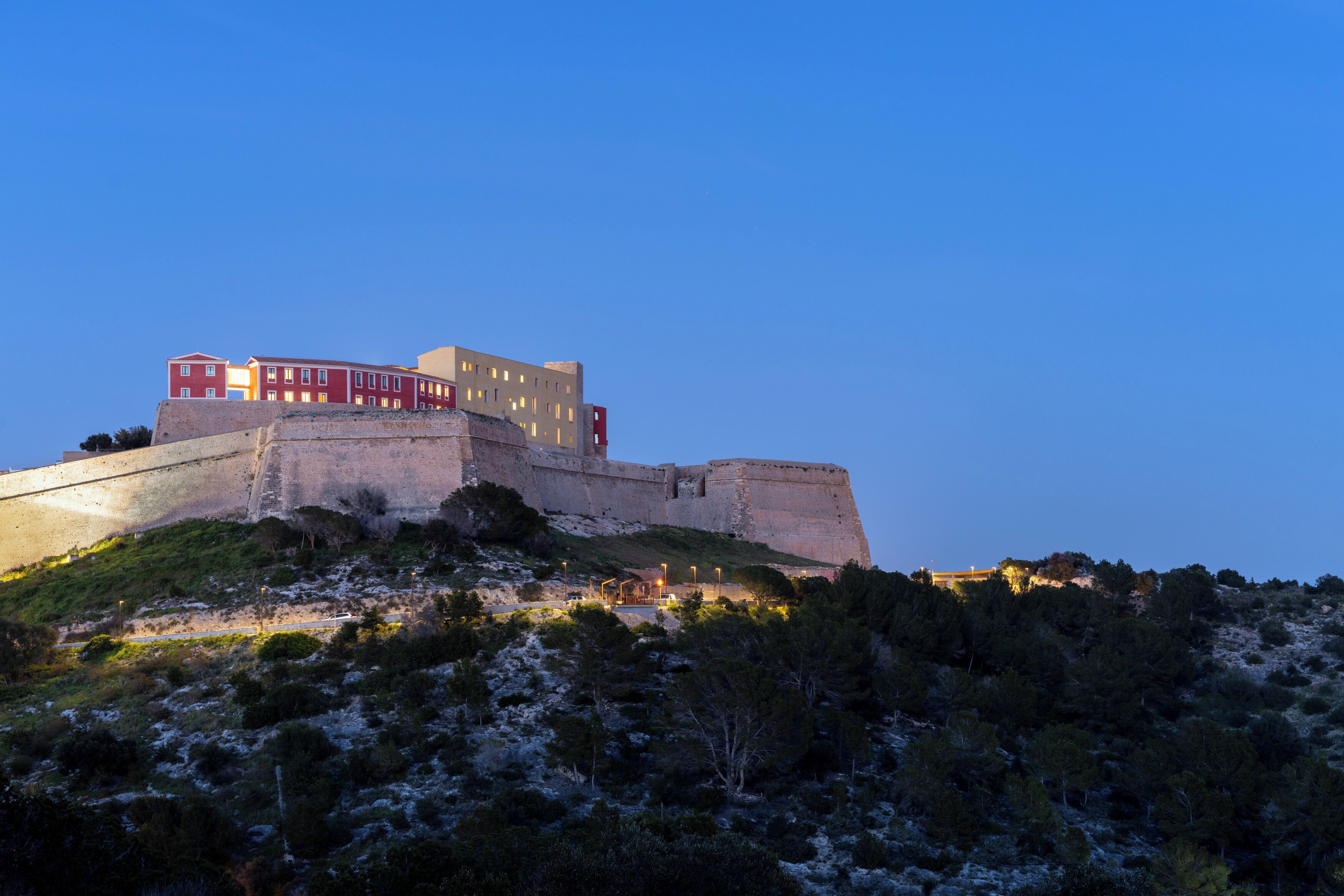 A historic building with multiple levels, situated on a hill with surrounding vegetation.
