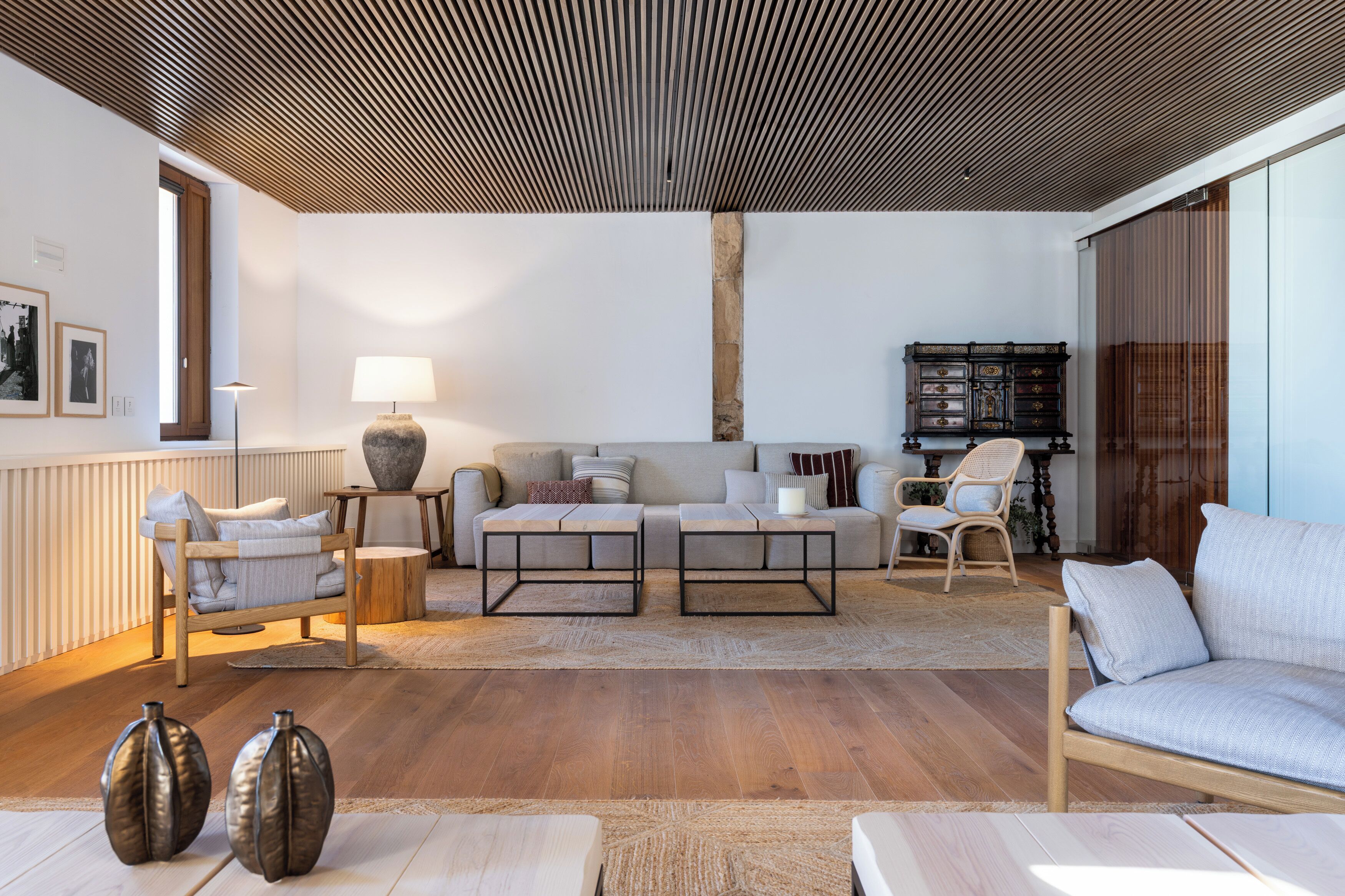 Una sala de estar moderna con techo de madera, un sofá, dos mesas auxiliares y una estantería.
