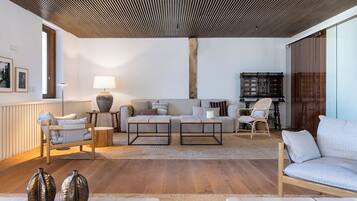 Una sala de estar moderna con techo de madera, un sofá, dos mesas auxiliares y una estantería.