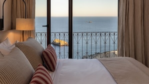 Habitación de hotel con una cama grande, vistas al mar y un balcón con barandilla.