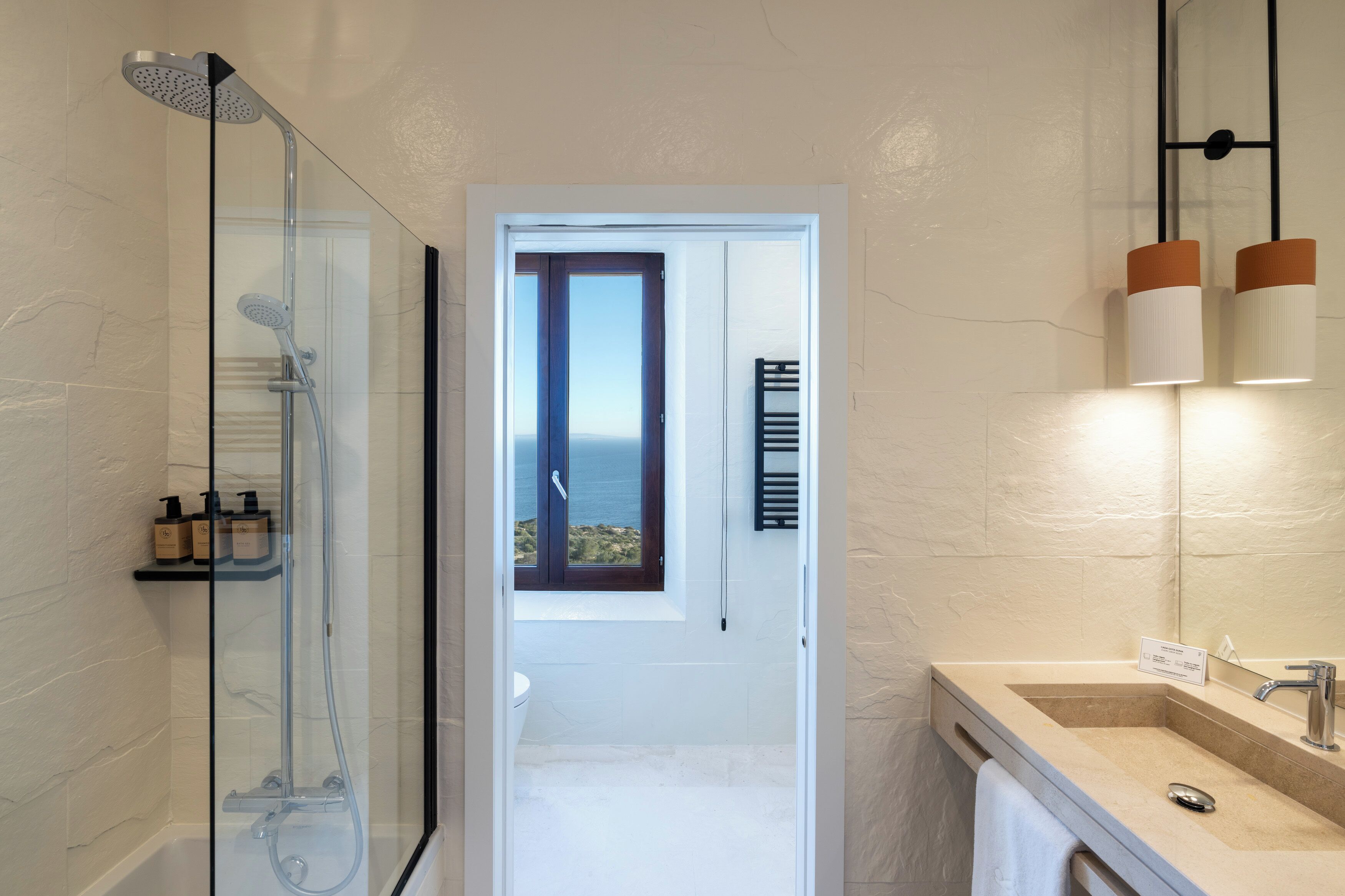 A bathroom with a glass-enclosed shower, a sink with a mirror, and a view through a door.