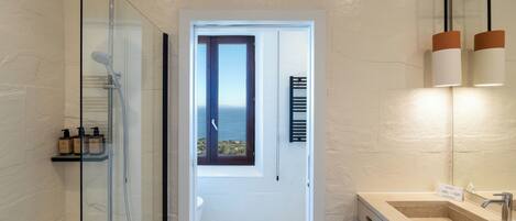 A bathroom with a glass-enclosed shower, a sink with a mirror, and a view through a door.