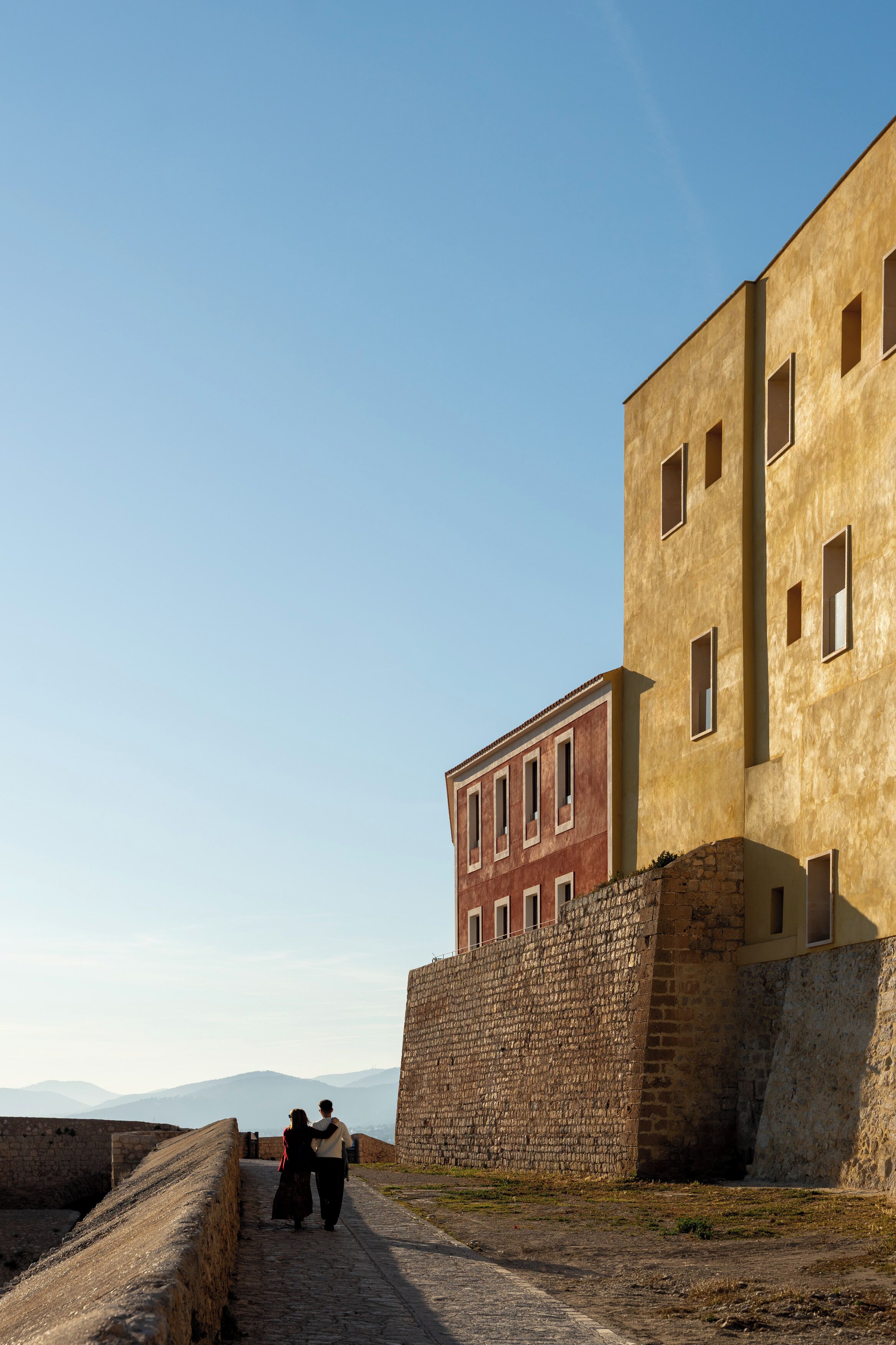 A historical building with a stone wall and a paved pathway.